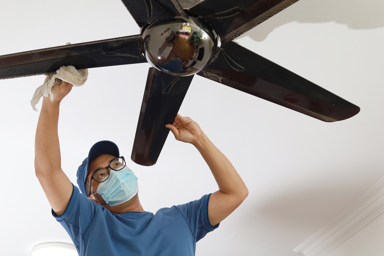 Asian man cleaning ceiling fan at home